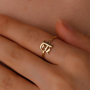Puede incluir: Un anillo dorado con una sola letra inicial, "A", en una fuente cursiva.