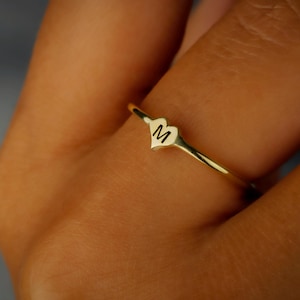 May include: A gold ring with a heart-shaped design featuring the letter "M" engraved on it.
