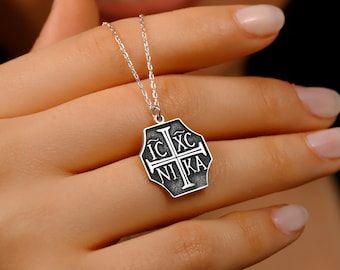 Puede incluir: Un collar de cadena de plata con un colgante de plata que presenta una cruz negra con la inscripción "IC XC NIKA" en forma octogonal.