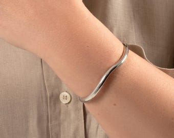Puede incluir: Un brazalete curvo de plata en la muñeca de una persona.