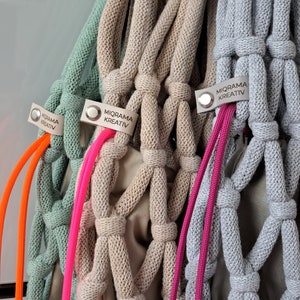 Puede incluir: Tres bolsas de cuerda tejidas a crochet con asas de diferentes colores. Las bolsas son verde claro, beige y gris claro. Cada bolsa tiene una etiqueta que dice "MIORAMA KREATIV".