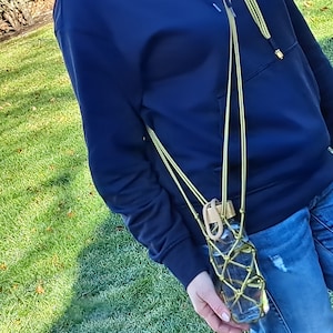 May include: A person wearing a navy blue hoodie with a gold chain holding a clear water bottle in a gold mesh bag.