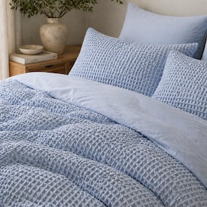 May include: A bed with light blue bedding, including a duvet cover and pillows. The duvet cover and pillowcases have a textured, waffle-weave pattern. The bed is neatly made, suggesting a focus on bedroom decor and textiles.