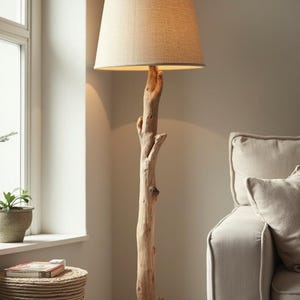 May include: A tall, natural wood floor lamp with a beige linen shade. The lamp's base is a thick, textured branch, and the shade is a classic tapered shape. The lamp is in a neutral-toned living room.