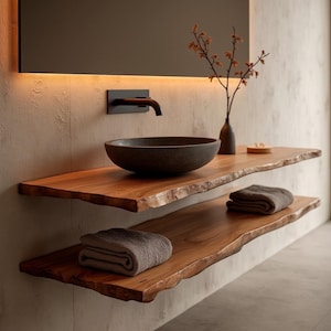 Könnte beinhalten: Modernes Badezimmer-Waschbecken mit einem dunklen Steinwaschbecken und einem schwarzen Wasserhahn. Das Waschbecken verfügt über zwei Regale aus Holz mit natürlicher Kante und gefalteten Handtüchern. Ein Spiegel und eine Vase ergänzen das minimalistische Design.