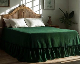 May include: A bed with a woven headboard and a dark green bedspread. Two white pillows rest on the bed. The bedspread has a ruffled skirt. The room has a natural, airy feel with sunlight streaming through the window.