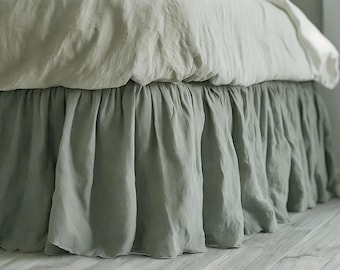 May include: A bed featuring a sage green bed skirt and a white and sage green duvet cover. The bed skirt is gathered, with a flowing, textured look. The bedding appears to be made from a soft, natural fabric.