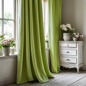 May include: Lime green linen curtains frame a window with a view of the outdoors. Pink roses in white ceramic pots sit on the windowsill. A white distressed chest of drawers holds more pink roses, creating a bright and airy interior design.
