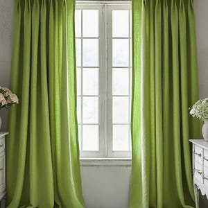 May include: Bright green curtains frame a white window, creating a vibrant contrast. The curtains are made of a soft fabric and are draped in elegant folds. Two white antique dressers with floral arrangements sit on either side of the window.