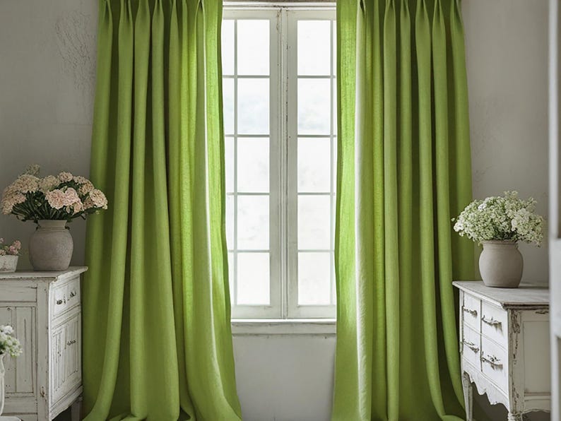 May include: Bright green curtains frame a white window, creating a vibrant contrast. The curtains are made of a soft fabric and are draped in elegant folds. Two white antique dressers with floral arrangements sit on either side of the window.