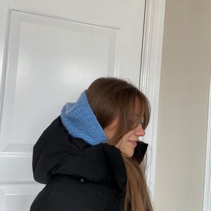 Puede incluir: Una mujer con una chaqueta acolchada negra y un gorro de punto azul claro.