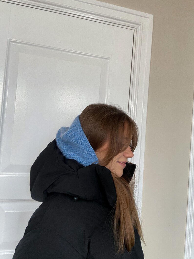 Puede incluir: Una mujer con una chaqueta acolchada negra y un gorro de punto azul claro.