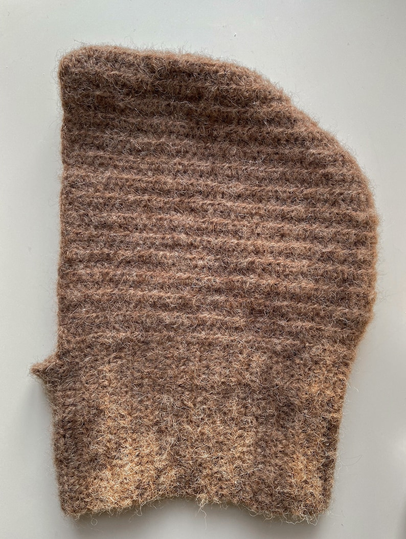 Op de afbeelding: Een bruine gebreide muts met een pluche textuur. De muts is gemaakt van een zacht, warm materiaal en heeft een geribbeld ontwerp.