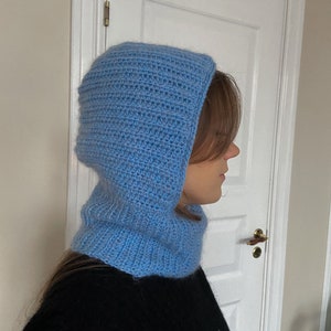 Puede incluir: Una bufanda de cuello de capucha de punto azul claro. La bufanda est&aacute; hecha a crochet y tiene un ajuste holgado y desgarbado.