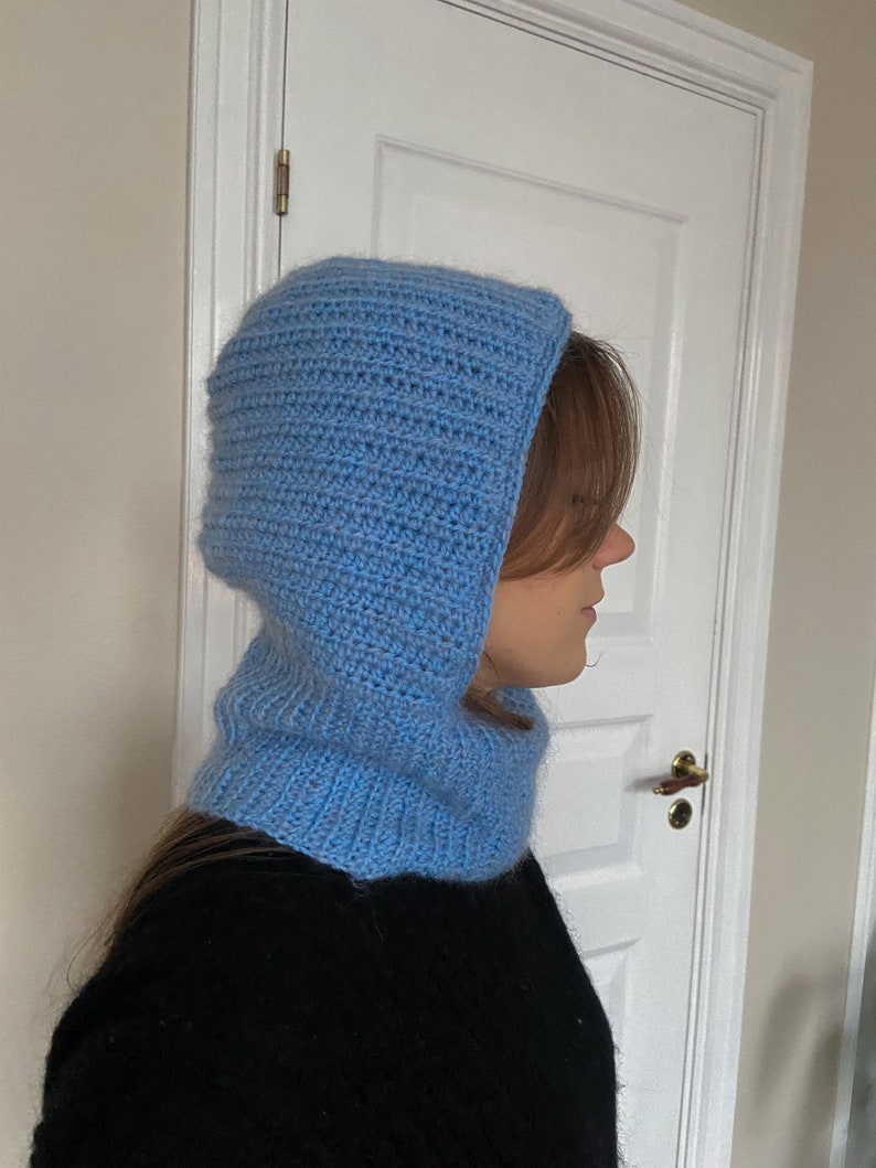 Puede incluir: Una bufanda de cuello de capucha de punto azul claro. La bufanda est&aacute; hecha a crochet y tiene un ajuste holgado y desgarbado.
