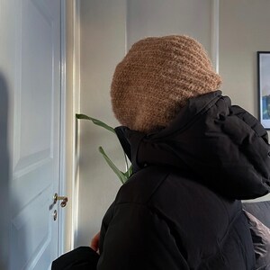 Op de afbeelding: Een persoon draagt ​​een bruine gebreide beanie en een zwart pufferjack.
