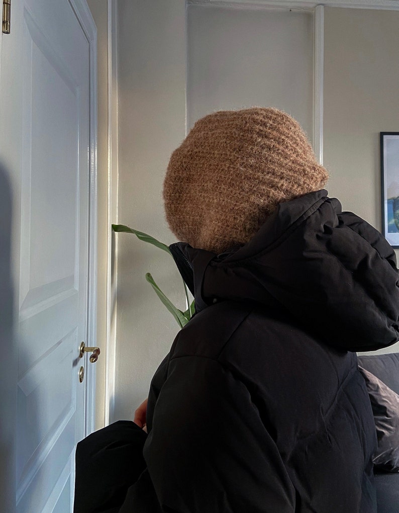 Op de afbeelding: Een persoon draagt ​​een bruine gebreide beanie en een zwart pufferjack.