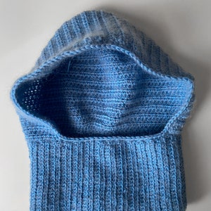 Puede incluir: Un cuello de lana con capucha de color azul claro tejido a crochet. El cuello de lana est&aacute; hecho con un hilo suave y tiene una textura acanalada.