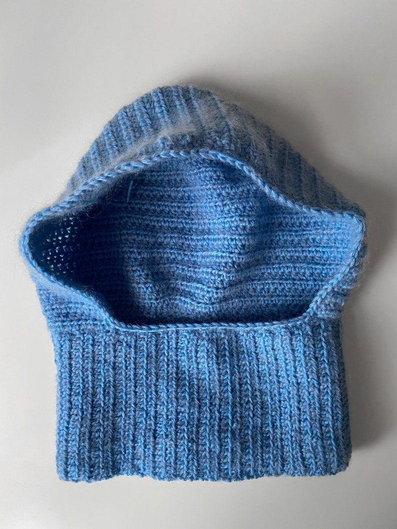 Puede incluir: Un cuello de lana con capucha de color azul claro tejido a crochet. El cuello de lana est&aacute; hecho con un hilo suave y tiene una textura acanalada.