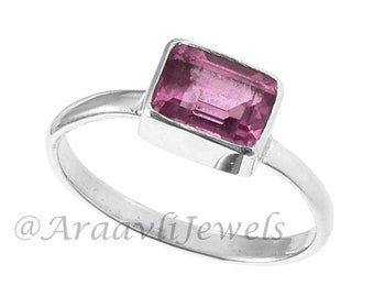 May include: A silver ring with a pink gemstone set in a rectangular bezel. The ring is simple and elegant.