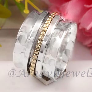 Könnte beinhalten: Ein silberner Drehring mit einem goldenen Band. Der Ring ist texturiert und hat eine gehämmerte Oberfläche. Das goldene Band ist ein Perlmuster.