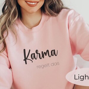 May include: Light pink sweatshirt with the text "Karma regelt das" in black.