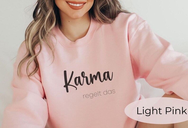 May include: Light pink sweatshirt with the text "Karma regelt das" in black.
