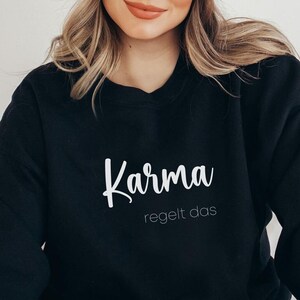 May include: Black sweatshirt with white text that reads "Karma regelt das".
