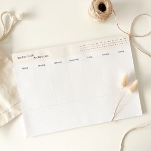 Könnte beinhalten: Ein weißer Wochenplaner mit einem gepunkteten Raster und dem Text "Another week Another plan" oben. Der Planer ist in sieben Spalten für jeden Tag der Woche unterteilt, beschriftet mit "Montag", "Dienstag", "Mittwoch", "Donnerstag", "Freitag", "Samstag" und "Sonntag".