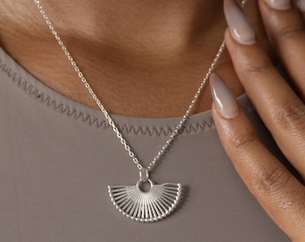 Puede incluir: Un collar de plata con un delicado colgante en forma de abanico. El colgante está hecho de alambres finos e interconectados que crean un diseño geométrico.