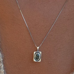 May include: A silver chain necklace with a square pendant featuring a dark green oval gemstone.
