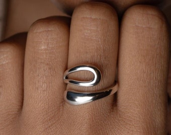 May include: A silver ring with a unique, abstract design. The ring is made from a single piece of metal that is bent and twisted to create a modern and stylish look.