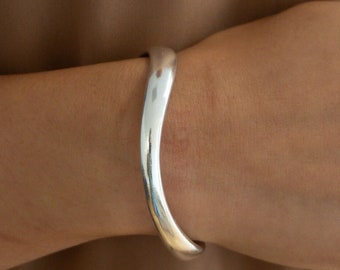 Puede incluir: Un brazalete de plata con un diseño curvo y liso.
