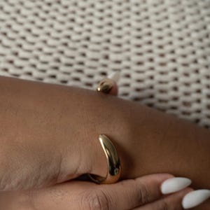 Puede incluir: Un brazalete abierto, curvado, de color dorado. El brazalete se lleva en la mu&ntilde;eca.