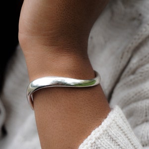 Puede incluir: Un brazalete de plata con un dise&ntilde;o ondulado. El brazalete se lleva en la mu&ntilde;eca.