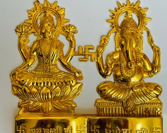 May include: Gold-colored metal sculpture of Lakshmi and Ganesha, Hindu deities, sitting on lotus flowers. The sculpture is on a base with the text "Jay Lakshmi Ma" and "Ganesh Ji" in Hindi.