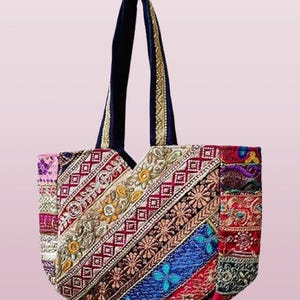 May include: A colorful tote bag with a patchwork design. The bag features a variety of embroidered fabrics in red, blue, gold, and purple. The handles are a dark blue velvet material with gold trim.