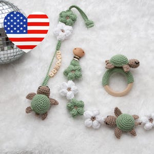 Könnte beinhalten: Ein gehäkeltes Babyspielzeug-Set mit einer grünen und weißen Blütengirlande, einem Holzring mit einer grünen gehäkelten Schildkröte und einem Holzklipp mit einer grünen gehäkelten Schildkröte und dem Namen "Valerie" in Holzperlen.