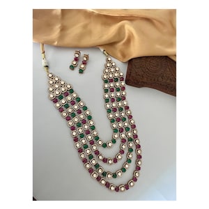May include: A four-strand gold necklace with green and pink square-shaped stones and white pearls. Matching earrings are included.