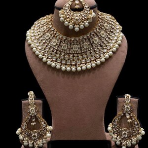 Pu&ograve; includere: Un set di collane da sposa indiane in oro e bianco con accenti di perle. Il set include una collana choker, orecchini e un maang tikka.