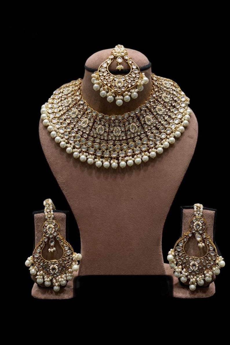 Pu&ograve; includere: Un set di collane da sposa indiane in oro e bianco con accenti di perle. Il set include una collana choker, orecchini e un maang tikka.