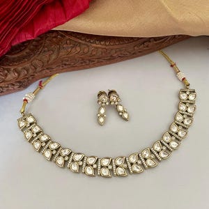 May include: A gold necklace and earrings set with a teardrop-shaped design. The necklace is made of small, clear stones set in gold metal. The earrings are also made of gold metal and have a teardrop-shaped design.