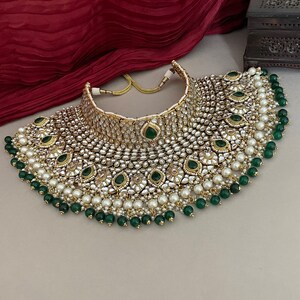 May include: A large, ornate gold necklace with white pearls and green gemstones. The necklace has a layered design with a central section of larger gemstones and a cascading fringe of pearls and gemstones.