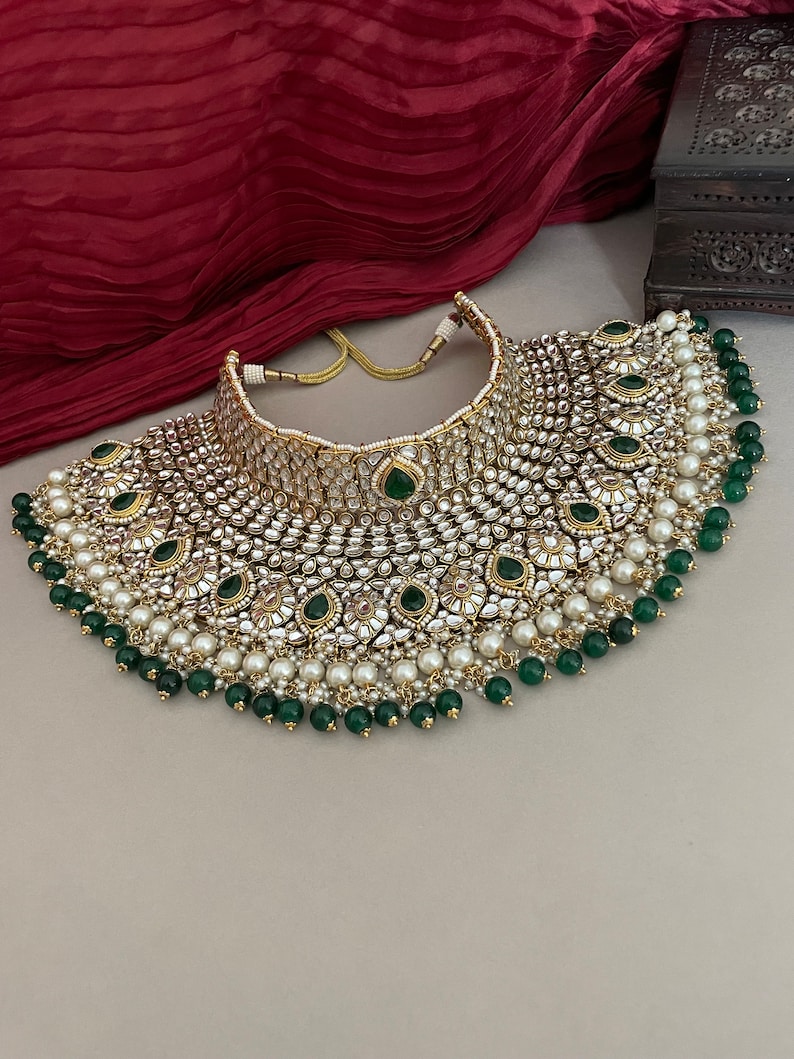 May include: A large, ornate gold necklace with white pearls and green gemstones. The necklace has a layered design with a central section of larger gemstones and a cascading fringe of pearls and gemstones.