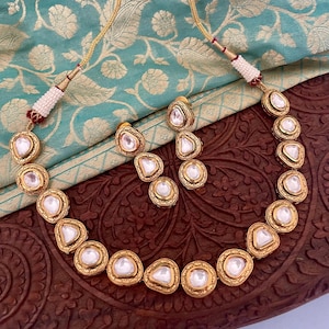 May include: A gold necklace and earrings set with white stones. The necklace has a chain with a series of oval-shaped stones, each with a gold border. The earrings are drop earrings with three oval-shaped stones.