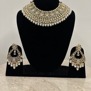 Pu&ograve; includere: Un set da sposa di collana e orecchini in oro e bianco con accenti di perle. La collana &egrave; un design multistrato con un grande ciondolo rotondo al centro. Gli orecchini sono a forma di lacrima con un design simile a quello della collana.