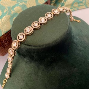May include: A gold bracelet with a row of round, clear stones set in a circular design.