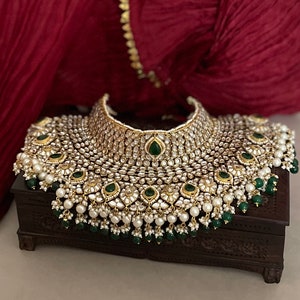 May include: A large, ornate gold necklace with white and green stones. The necklace is on a dark wooden box.