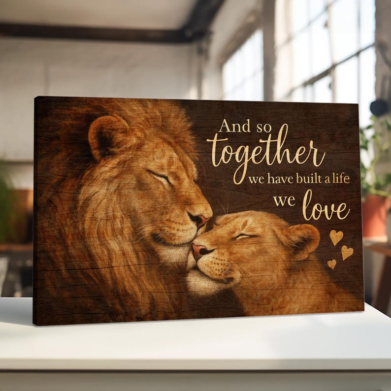 May include: A canvas print with a woodgrain background featuring two lions, a male and a female, with their heads touching. The text "And so together we have built a life we love" is written in gold lettering on the canvas.