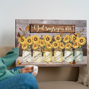 May include: A wooden wall art piece featuring sunflowers in mason jars with the words "Unique," "Special," "Lovely," "Precious," "Strong," and "Chosen." The phrase "God says you are" is above the jars. Butterflies are scattered throughout.